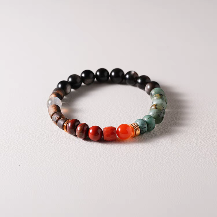 Nirvana Lumière Handmade Earth Energy Bracelet displayed on a wooden surface – A handcrafted gemstone bracelet with Black Agate, Green Jasper, and Orange Carnelian.