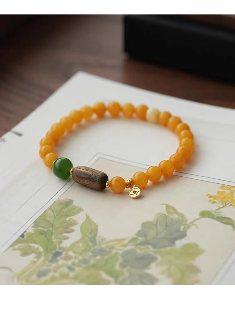 Close-up of Yanyan bracelet featuring yellow jade, green aventurine, and wooden beads with gold accents on a white background.